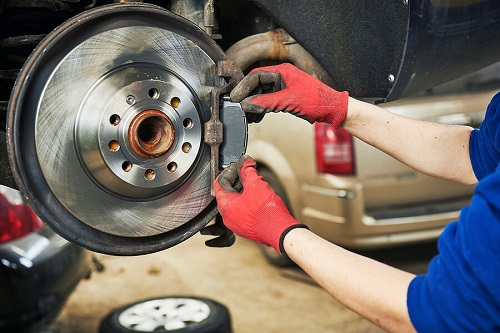 Brake Pad Repair by ABS Unlimited in Fairfax VA. Closeup image of a car mechanic doing automobile brake pads replacement in a car garage shop.