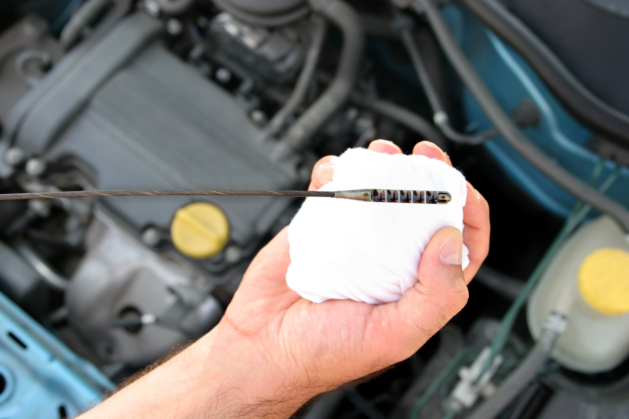 mechanic hand holding white cloth and the end of an oil dipstick to check the oil