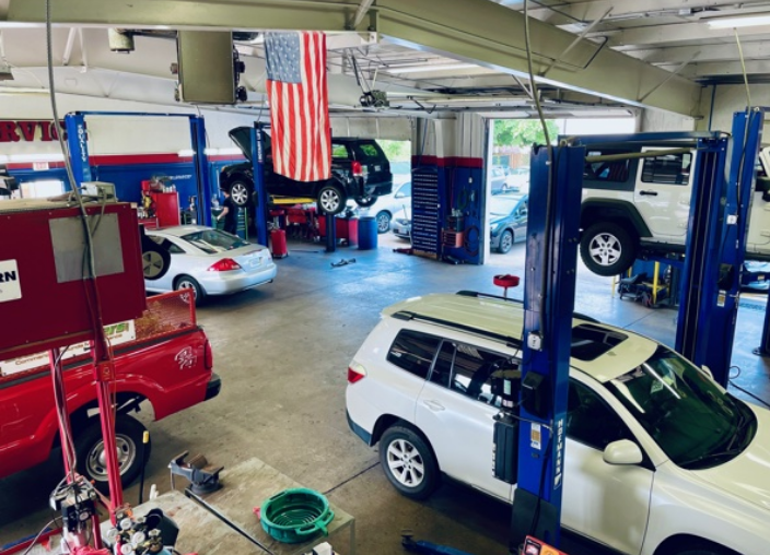 inside of ABS Unlimited Auto Repair shop bay area with cars on lifts and American flag hanging from the ceiling