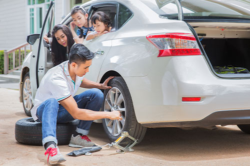 Prepare Your Car for Summer Road Trips | ABS Unlimited in in Fairfax, VA. Image of Father change tire for family trip