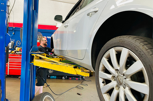 Winter Maintenance Package | ABS Unlimited Auto Repair | Fairfax Auto Repair. Image of white sedan on lift in shop while male technician is checking driver side tire.