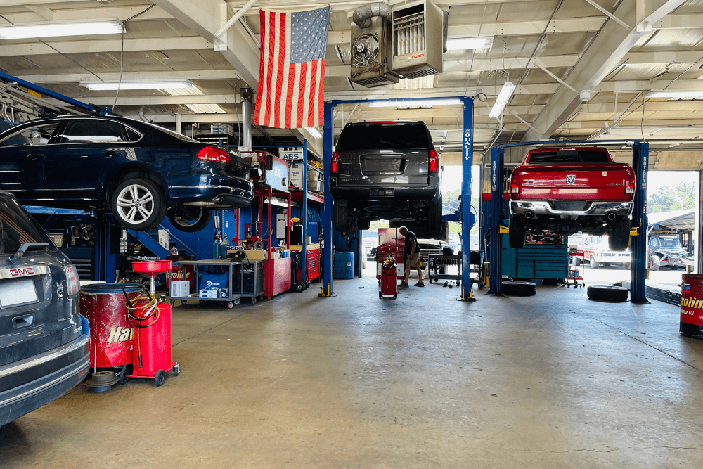 Back-to-school car maintenance, auto repair in Fairfax, VA by ABS Unlimited Auto Repair. Image of multiple vehicles lifted in a clean shop with an American flag overhead, reflecting the shop’s dedication to safety, performance, and professional service.